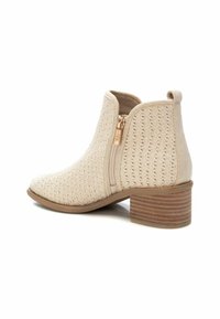 Bota de tobillo beige con tejido texturizado, cremallera lateral con herrajes dorados y un tacón marrón apilado. Diseño de puntera redonda.
