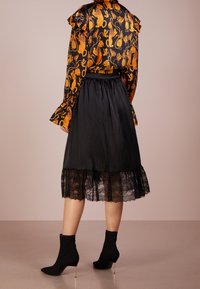 Blouse à manches longues avec un motif floral orange, jupe noire en satin avec bord en dentelle, et bottines noires à bout pointu avec des talons aiguilles.