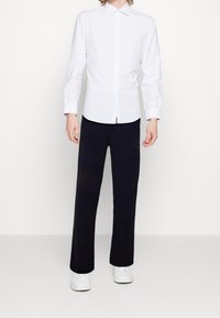 White button-up shirt with thin navy stripes, long sleeves, paired with loose black trousers and white sneakers. Simple and classic design.