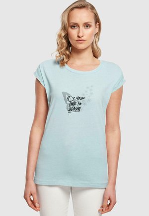 Lyseblå bomulls T-skjorte med korte oppbrettede sleeves, som har et sommerfuglmotiv og teksten "Det er din tid til å blomstre" i svart.