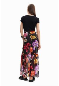 Haut noir ajusté associé à une jupe maxi florale à volants avec des fleurs vibrantes et multicolores sur un fond noir, finie par des bords froncés.