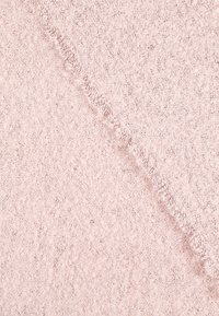 Gros plan sur un tissu doux et texturé avec une couture diagonale effilochée, dans des tons rose pâle.