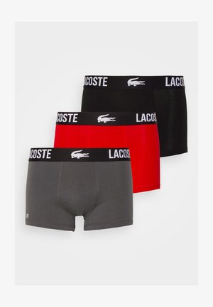 Três pares de boxers masculinos: cinza, vermelho e preto. Cada um apresenta uma faixa preta na cintura com o logotipo da Lacoste em branco. Tecido suave, design simples.