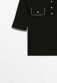 Zwart geribd stoffen T-shirt met korte mouwen en gouden knopen, voorvak met overslag afgezet met wit, en witte dubbele stiksels op de mouwzoom.