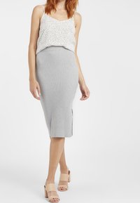 Gekürztes weißes Oberteil mit schwarzen Punkten, kombiniert mit einem gerippten grauen Midirock mit seitlichen Schlitzen und beigen Blockabsatzsandalen.