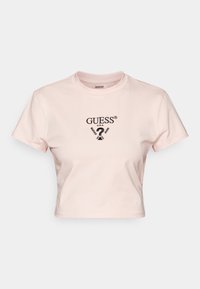 Zkrácený růžový tričko vyrobené z bavlny s kulatým výstřihem. Na přední straně je černé logo "GUESS?" a grafický potisk. Krátké rukávy.