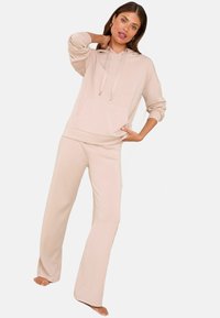 Heledad beež kapuuts ja vastavad laiad püksid, mis on valmistatud pehmest kangast. Kapuutsil on ees muttide tasku ja kuldsete aktsentidega tõmblukud.