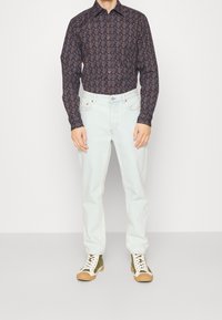 Chemise à manches longues à motifs foncés, associée à un jean droit bleu clair et des baskets montantes vertes avec des accents blancs et des semelles en caoutchouc.