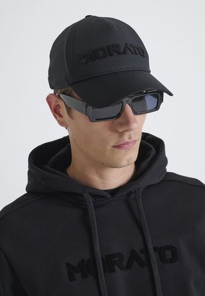 Casquette noire avec logo « MORATO » en relief, associée à des lunettes de soleil noires rectangulaires et à un sweat à capuche noir avec un logo texturé.