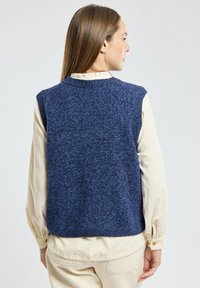 Granatowy, dzianinowy sweter bez rękawów o teksturowanym wykończeniu, okrągłym dekolcie i solidnym wzorze widocznym z tyłu, w połączeniu z jasnoszarym koszulą.