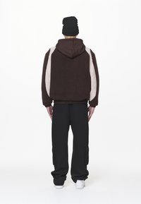 Felpa con cappuccio marrone con dettagli beige chiaro, orlo elastico e cappuccio. Abbinata a pantaloni cargo neri e sneakers bianche.