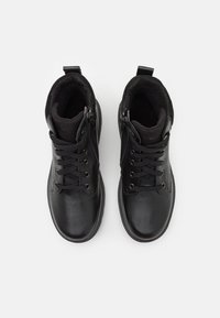 Botas negras con parte superior de cuero, acentos de ante texturizado y forro acolchado. Cuentan con cordones y cremalleras laterales para un fácil uso.