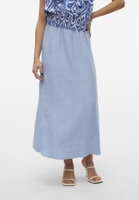Ljusblå maxikjol i mjukt tyg med en slät textur och en flödande silhuett. Kombinerad med en mönstrad blå och vit topp.