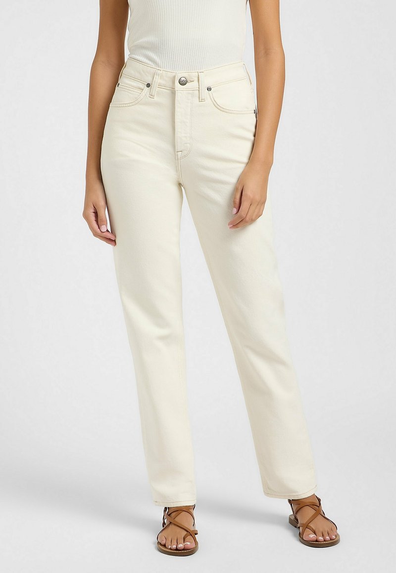 Jeans blancs taille haute en coupe droite, faits de denim doux avec des boutons en métal argenté et des poches avant. Associés à des sandales brunes à lanières.