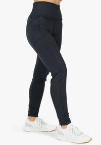 Leggings neri a vita alta con una texture liscia e cuciture a contrasto, abbinati a scarpe da ginnastica bianche con accenti grigi.