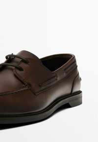 Brown leather shoe featuring a lace-up design, rounded toe, and subtle stitching details. The sole is flat and slightly textured.
