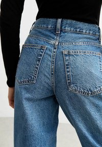 Light blue denim jeans with a high waist, featuring two back pockets and visible stitching details. The fabric has a textured appearance.