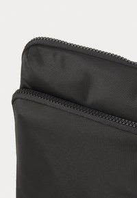 Schwarze Nylon-Tasche mit zwei Reißverschlussfächern, ausgestattet mit einer strukturierten Oberfläche und robusten Reißverschlüssen für sicheren Verschluss und einfachen Zugriff.