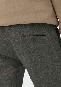 Grijze geruite broeken hebben een elegante uitstraling met een enkele achterzak, knoopsluiting en een zachte textuur. De stof vertoont subtiele kleurvariaties.