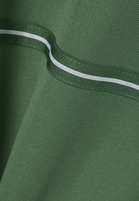 Tela verde con un acabado texturizado, que presenta una franja blanca a lo largo de la costura. El material muestra un patrón de tejido sutil.