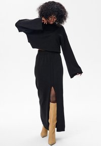 Czarny dzianinowy krótki top z szerokimi rękawami zestawiony z długą czarną spódnicą z bocznym rozcięciem. Noszony z jasnobrązowymi wysokimi kozakiem do kolan.