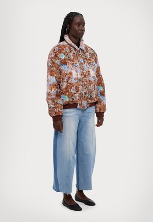 Puffy brun og blå mønstret jakke med høj krave, parret med brede lyseblå jeans og sorte flade sko. Tekstureret stof med lommer.