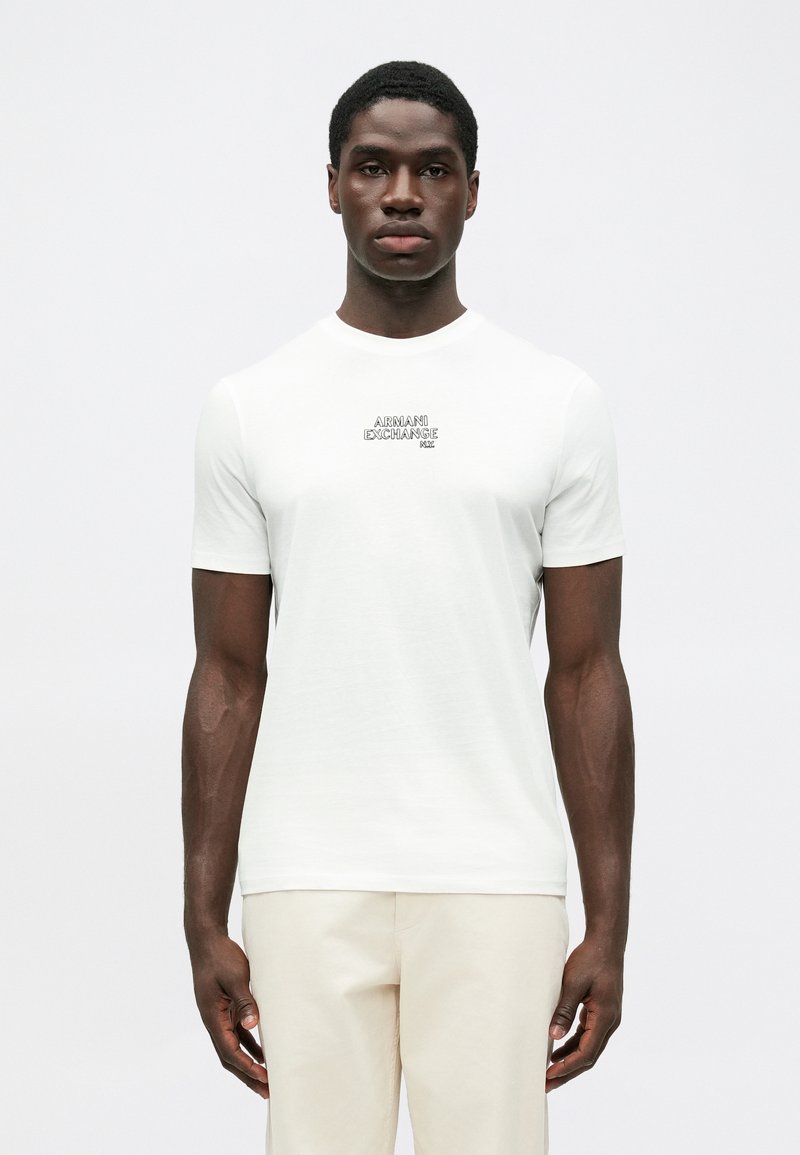Bílý tričko s krátkým rukávem vyrobené z měkkého materiálu, s jemným logem "Armani Exchange" v černé barvě na hrudi. Hladká textura.