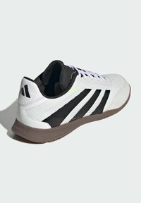 Witte en zwarte low-top sportschoen met zwarte strepen, bruine zool, witte veters en een gewatteerde zwarte kraag, weergegeven in een schuin rechts aanzicht.