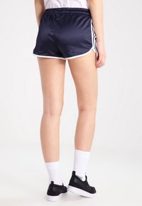 Námořnické saténové šortky s bílým lemem, s elastickým pasem a sportovním střihem. Nosené s černými teniskami a bílými ponožkami.