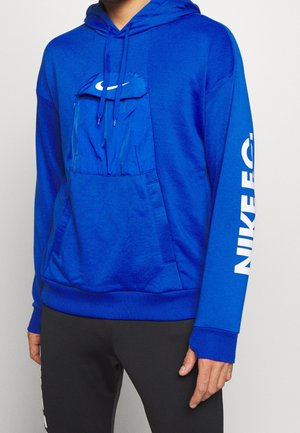 Haut à capuche bleu avec une poche avant et une capuche, arborant un logo Nike blanc sur la poche et des lettres le long de la manche. Texture douce.