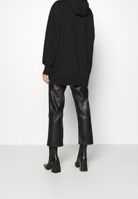 Sudadera negra oversized con textura suave, combinada con pantalones de cuero negros de cintura alta y botines de tacón altos con tacón cuadrado.