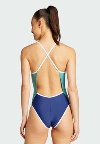 Uimapuku yhdestä kappaleesta, jossa on teal- ja tummansininen värimaailma. Siinä on korkea selkä ja ristiselkästrapit, valkoisella reunustettuna kontrastia varten.