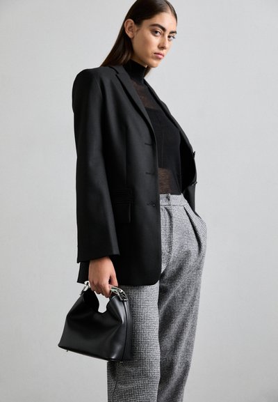 Schwarzer Blazer mit lässiger Passform, schwarzes Oberteil mit hohem Kragen darunter, graue karierte Hose und eine kleine schwarze Handtasche mit silberner Hardware.