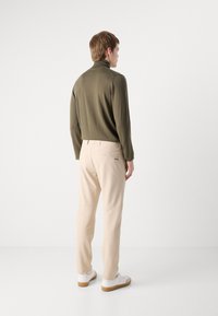 Olive green, long-sleeve turtleneck paired with light beige, tailored pants. Shoes are white with a gum sole. Simple, modern design.