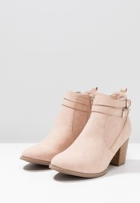 Des bottines en daim rose clair à bout pointu, fermeture éclair sur le côté, accents perforés et talon en bois empilé.