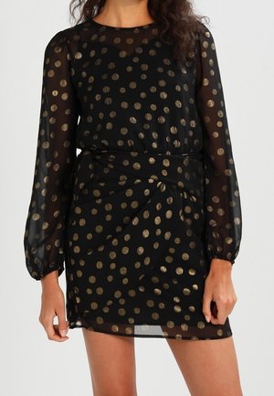 Czarna przezroczysta sukienka mini z długim rękawem, ozdobiona metalicznymi złotymi groszkami, z marszczonym paskiem w talii, prezentowana na stojącej osobie.
