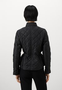 Black quilted jacket featuring a fitted design, high collar, long sleeves, and a cinched waist; smooth texture with a diagonal pattern.