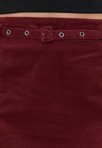 Bordeaux corduroy rok met een veilige tailleband voorzien van metalen oogjes en een stoffen riem. Textuur oppervlak met een verticale ribbelpatroon.