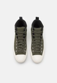 Vysoké tenisky v olivově zelené plátno s černými akcenty, s kulatými bílými gumovými špičkami a tradičním šněrováním.