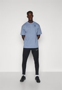 Lysblå kortærmet skjorte med et rutemønster, parret med sorte slim-fit bukser med et hvidt Nike-logo og sorte sneakers.