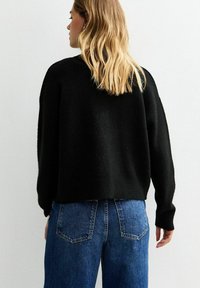Zwarte cropped trui met een zachte textuur, voorzien van lange mouwen en een ronde halslijn, gecombineerd met high-waisted blauwe spijkerbroek.