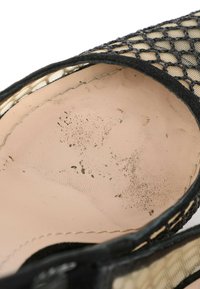 Gros plan de l’intérieur d’une chaussure montrant une semelle intérieure beige avec une tige noire texturée et des taches de saleté visibles sur la surface de la semelle.