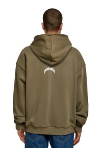 Hanorac supradimensionat de culoare verde măsliniu, cu glugă mare, textură moale și design tipărit pe spate. Asortat cu blugi din denim albastri.