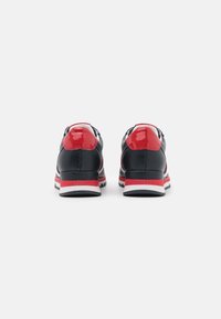 Zapatillas con un cuerpo de malla perforada negra, acentos rojos brillantes, una mediasuela blanca y una suela texturizada negra con rayas rojas.