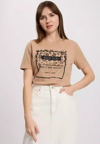 Brązowy T-shirt z czarnym napisem "WILD GIRL", akcenty w panterkę, krótkie rękawy i luźny krój. W zestawie z białą spódnicą.
