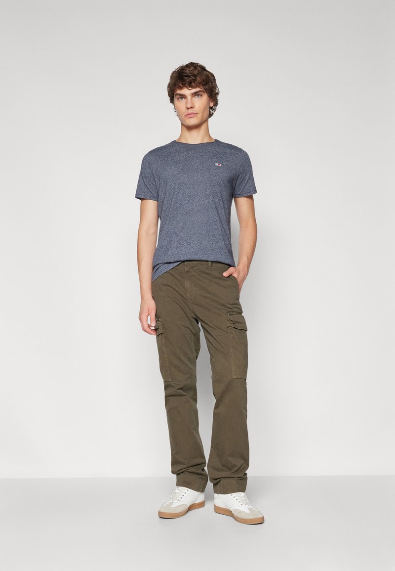 Marinblå heather crew-neck t-shirt, olivgröna cargo-byxor med sidofickor och vita sneakers med beige detaljer. Enkel, ren design.