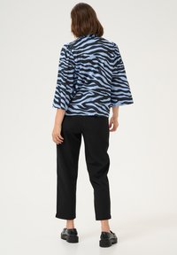 Top a righe zebrate blu e nere con maniche a tre quarti, abbinato a pantaloni neri e scarpe chunky nere. Tessuto dalla texture liscia.