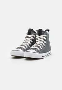 Oblečené tenisky s vysokým střihem z šedé plátěné látky s bílým gumovým špičkou. Mají bílé tkanice, černé očky a texturovaný povrch na svršku.