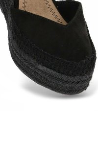 Espadrilles de ante negro con suela de yute trenzado. Presentan una punta afilada y un sutil detalle de costura a lo largo del borde cortado de la parte superior.