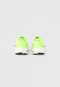 Αθλητικά παπούτσια σε νέον πράσινο με επάνω μέρος από αναπνεύσιμο πλέγμα, μαξιλαρωμένη σόλα και εξωτερική σόλα από μαύρο καουτσούκ· διαθέτουν μινιμαλιστικό σχεδιασμό και λογότυπα ως διακοσμητικά στοιχεία.